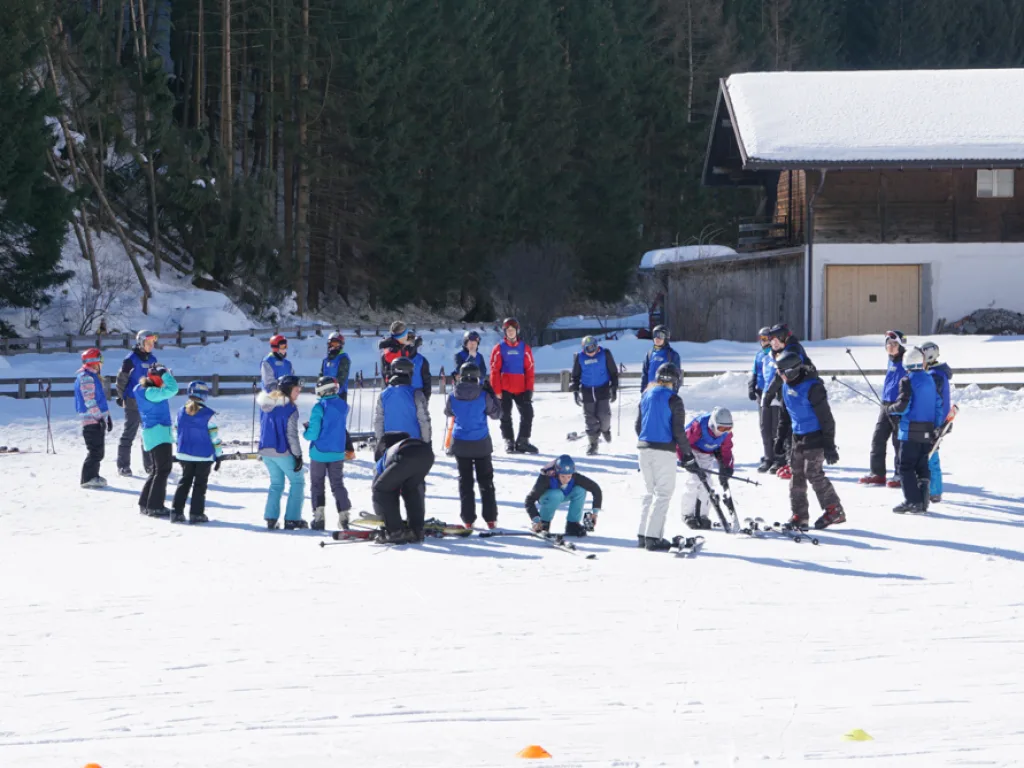 Skigruppen sammeln sich vor den Häusern am Pistenrand.